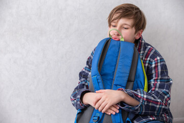 Boy sits with backpack, showing signs of fatigue while contemplating his surroundings in a quiet room during the afternoon