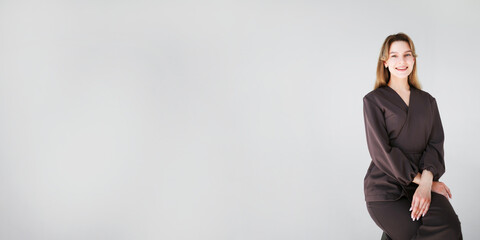 Wide banner with a smiling female doctor in dark uniform sitting on a stool on white background with copy space for text or design.