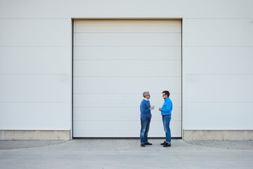 Two Men Engaged in Conversation Outside Industrial Building with White Walls