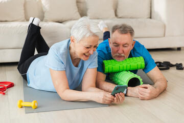 Yoga fitness training online. Senior couple practicing yoga fitness with online lessons on smartphone. Old wife husband watching training on phone before workout. Family doing sports exercise at home