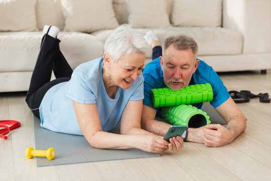 Yoga fitness training online. Senior couple practicing yoga fitness with online lessons on smartphone. Old wife husband watching training on phone before workout. Family doing sports exercise at home - Powered by Adobe