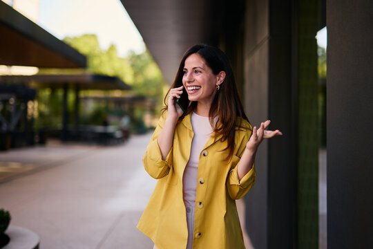Smiling Woman Talking on Smartphone Outdoors in Stylish Yellow Coat