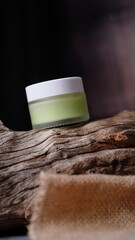 small glass jar with white cap containing light green liquid substance rests against piece of...