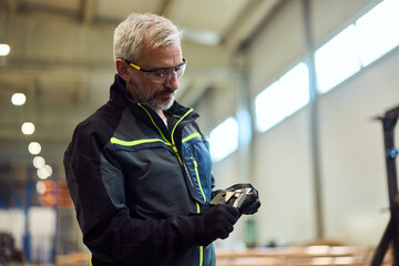Worker Examines Metal Component in Industrial Factory Setting With Safety Equipment