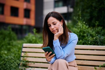 Woman Sitting on Bench Using Smartphone in a Green Urban Setting