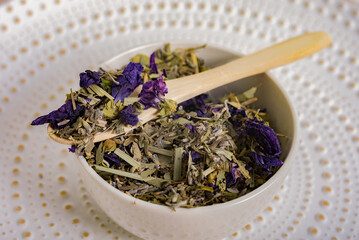 Close-up of a wooden spoon with herbal tea on a plate with a mountain of various dried herbs and...