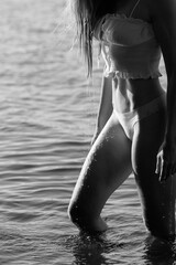 woman wades through the shallow water of a lake, her figure illuminated by sunlight. Water droplets cling to her skin, creating a tranquil and serene atmosphere perfect for relaxation