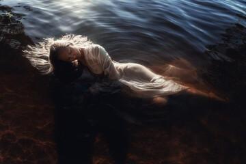 woman in a flowing white dress relaxes in calm waters, surrounded by nature. soft light of the golden hour casts a peaceful glow over her serene pose and the gentle ripples