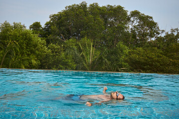 person enjoys leisure time by floating in a tranquil swimming pool. Vibrant green trees surround...