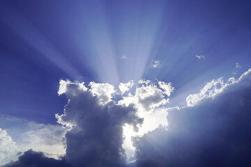 Sun rays break dramatically through thick, white clouds in the blue sky, dense clouds slide in...