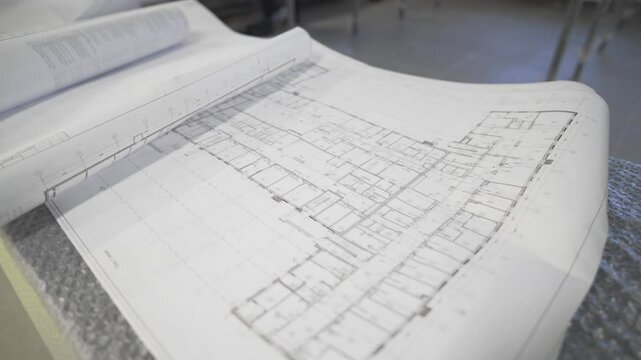Open blueprints stretch across drafting table. Architectural layout shows clear lines and building plans. Detailed construction drawings