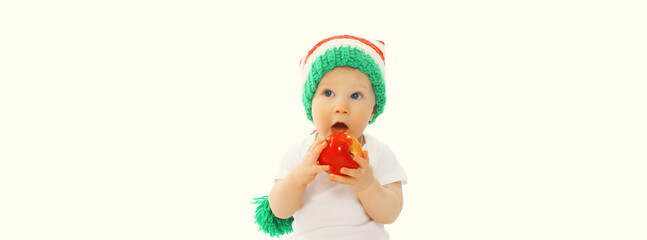 Cute baby eating red apple fruit or playing wearing colorful hat on white studio background