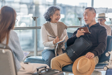 happy asian senior couple passengers,waiting for boarding in the airport terminal,enjoy talking together,elderly woman taking note something on notebook and smiling happily