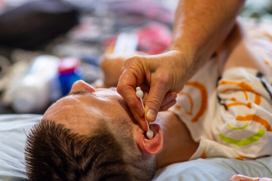 Middle aged woman cleaning ears of son with disability with cotton tips