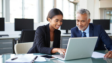 Photo of a young businesswoman and a mature businessman collaborate on a laptop in a modern office setting