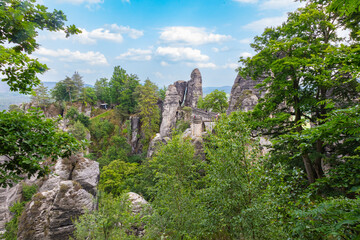 Scenic view of the Bastei Bridge in Saxon Switzerland National Park near Rathen, Germany, surrounded by dramatic sandstone rocks and lush forest under a bright summer sky.
