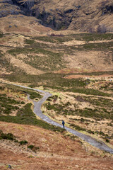 A solitary figure traverses the rugged, winding path through the majestic and mist-shrouded peaks of the Scottish Highlands, possibly in the iconic Glen Coe, where ancient landscapes meet dramatic ski