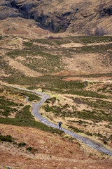 A solitary figure traverses the rugged, winding path through the majestic and mist-shrouded peaks of the Scottish Highlands, possibly in the iconic Glen Coe, where ancient landscapes meet dramatic ski