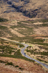 A solitary figure traverses the rugged, winding path through the majestic and mist-shrouded peaks of the Scottish Highlands, possibly in the iconic Glen Coe, where ancient landscapes meet dramatic ski