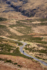 A solitary figure traverses the rugged, winding path through the majestic and mist-shrouded peaks of the Scottish Highlands, possibly in the iconic Glen Coe, where ancient landscapes meet dramatic ski
