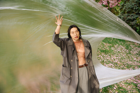 Stylish young man in grey outfit poses creatively in a vibrant park setting