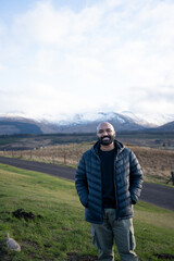 A guy in a scenic view of a road leading into a vast, rugged landscape with snow-capped mountains under a cloudy sky, likely in the Scottish Highlands