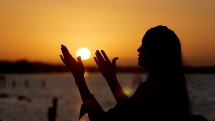 Woman worshipping god at sunset with open arms