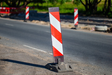road construction barrier with red and white stripes on asphalt street during sunny day traffic safety sign equipment marking construction area in city roadwork site infrastructure improvement work