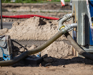 industrial hoses connected to pump machine at construction site with sand piles and dirt ground...