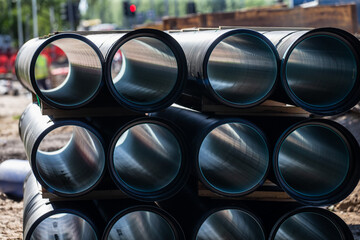 stack of large black metal pipes at construction site with blurred background showing building...