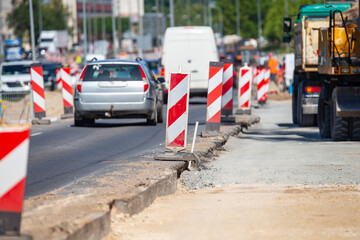 road construction site with red and white safety barriers cars passing by and heavy machinery...
