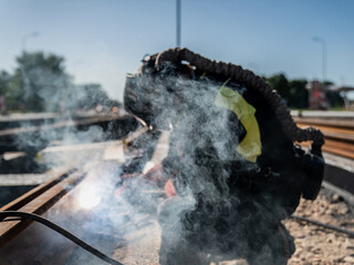 Welder working on steel rails with arc welding torch producing smoke and sparks in outdoor...