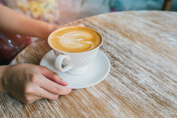Coffee in cafe. Warm Coffee Cup on Rustic Table with Hands Holding Mug in Cozy Cafe Setting