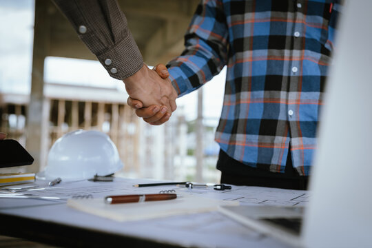 Two builders shaking hands at a construction site, representing a successful agreement and partnership built on trust, cooperation, and a shared goal of developing and growing real estate.
