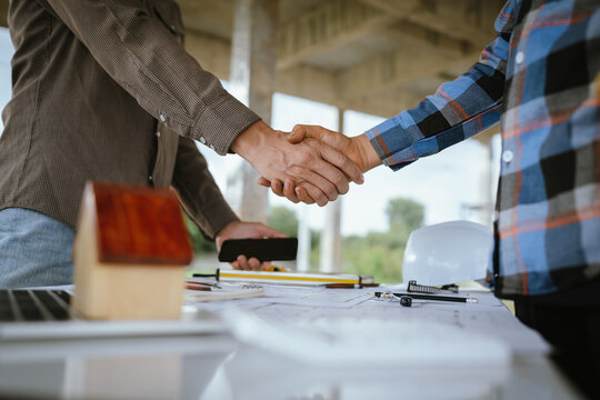 Two builders shaking hands at a construction site, representing a successful agreement and partnership built on trust, cooperation, and a shared goal of developing and growing real estate.