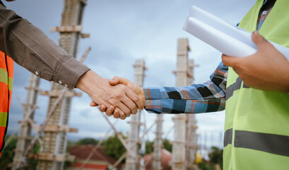 Two builders shaking hands at a construction site, representing a successful agreement and...