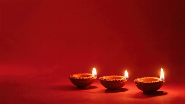 Three traditional Diwali oil lamps glowing on a plain red background, minimalist festive concept with space for text