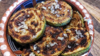 Grilled zucchini slices with garlic and pepper in rustic bowl.