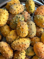 Close up of multiple horned melons kiwano with spiky orange-yellow skin in a metal tray. Exotic fruit concept, tropical food, healthy nutrition, and superfood market