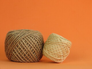 Roll of thick ecru sewing thread and roll of jute rope on orange background.	