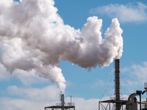 Plumes of steam rising from industrial chimneys into a blue sky