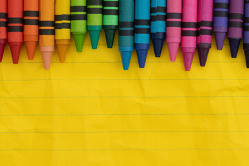 Crayons with yellow ruled loose leaf notebook paper background