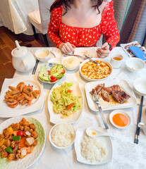 Woman enjoying traditional chinese food at restaurant, A european girl in a red dress sitting at a table with a variety of Asian dishes, smiling and relaxed.