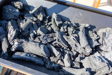 Charcoal pieces in a black metal tray under sunlight
