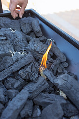 Hand igniting charcoal with a small flame