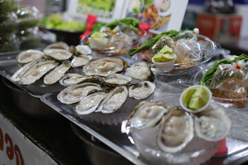 Fresh oysters on ice displayed at a seafood market stall, served with lime, herbs, and sauces in a vibrant and appetizing street food setting.
