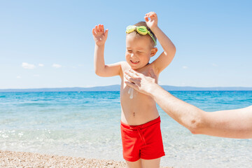Father applying sunscreen to child at the beach on a sunny day