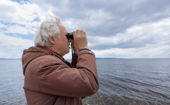 Senior man looking through binoculars at the beach under a thundery sky