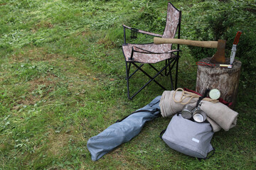 Hiking. Things and objects for tourism and survival in the forest or mountains. On the grass near the stump lie an axe, matches, canned food, rope, a tourist chair, a backpack and other things