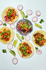 Tacos on corn tortillas with beef, chicken and vegetable fillings on a white background with lime wedges